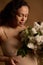 Close-up gorgeous gravid woman in beige lingerie, holding bouquet of blooming lilacs. Pregnancy fashion. Body positivity