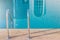 Close up grab bars ladder with blue water in swimming pool in the background.