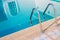 Close up grab bars ladder with blue water in swimming pool in the background.