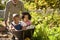 Close Up Of Grandchildren Pushed In Barrow By Grandfather Working In Vegetable Garden Or Allotment 