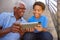 Close Up Of Grandfather With Grandson Sitting On Steps Outdoors At Home Using Digital Tablet