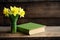 Close-up green book and a vibrant yellow daffodil on a rustic wooden table Generative AI