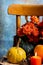 Close-up of green and orange pumpkins, candle and orange flowers on antique chair, gray background