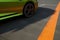 A close up of a green and orange sports car zooming around a wide turn on a slick asphalt surface. Speed drive concept