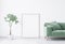 Close up for green velvet sofa with wooden base in modern interior space. White wall background with wooden frame and green plant