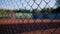 Close-up of the grid enclosing the tennis court. Silhouettes of people playing tennis are visible