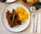 close up of grilled pigs trotter with fried potato and asparagus served on white plate on wooden table