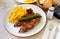 close up of grilled pigs trotter with fried potato and asparagus served on white plate on wooden table