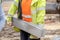 Close up of groundworker in orange and yellow hi-viz  carrying heavy concrete kerbs on construction site during new road