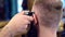 Close up of hair trimmer machine in cropped hands doing male hairstyle. Cutting hair near ear, brush shaking off hair