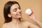 Close up half naked woman 20s with perfect skin nude make up applying facial cream isolated on beige pastel wall
