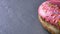 Close-up half-shot of delicious pink donut with multicolored chips and eyes spinning slowly on gray table background.
