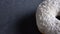 Close-up half-shot of delicious white donut with coconut chips spinning slowly on gray table background.