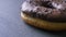 Close-up half-shot of glazed brown donut with chocolate chips spinning slowly on gray table background.