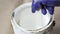 Close up of hand gloved painter mixing paint in metal paint can with wooden stick