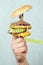 Close-up hand with a high-calorie big burger on a fork with a measuring tape . diet concept, unhealthy eating and