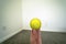 Close up of a hand holding a baseball against white wall and dark floor