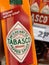 Close up of hand holding bottle of spicy red Tabasco sauce in front of shelf in german supermarket