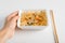 Close-up of hand holding box with ready-made instant Chinese noodles. Popular Asian dish and chopsticks