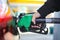 Close up hand holding green gasoline fuel nozzle and being fill gas tank of black car in gas station Concept of Global Fossil Fuel