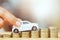 Close up hand holding model of toy car white on over a lot money of stacked coins - insurance, loan and buying car finance concept