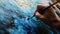 close up of hand holding painbrush drawing painting on canvas with blue color