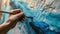 close up of hand holding painbrush drawing painting on canvas with blue color
