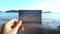 Close up hand holding photograph in front of beautiful tropical beach travel concept. Sun shining beautiful day