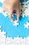 Close up hand holding and playing jigsaw game incomplete. White part of jigsaw puzzle pieces on blue background. concepts of