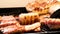 Close-up of hand holding tongs roasting pork ribs cut into small pieces on a pan on a picnic stove.