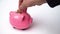 Close up of hand inserting coin into piggy bank. Saving money and financial education concept