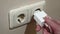 Close-up A hand inserts a phone charger into a white electrical socket