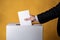 Close-up, a hand in a jacket holds a ballot near the box