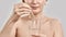 Close up of hand of middle aged woman holding dropper with medication and glass isolated over grey background