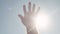 Close-up of hand reaching for sun. Stock. Bright sunlight breaks through fingers of outstretched hand to sky