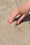 Close up on hand with red manicure finds seashell on sandy beach