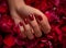 Close-up of a hand with red polished nails resting on a bed of vibrant red roses.