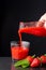Close-up of hand serving strawberry juice in glass cup on slate with strawberries, black background,
