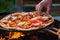 close-up of hand setting a wooden peel under a freshly grilled bbq pizza