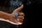 A close up of hand showing a thumbs up and smoky black background