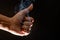 A close up of hand showing a thumbs up and smoky black background