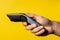 Close up on hand of unknown caucasian man holding electric beard trimmer cordless hair cutter in front of modern yellow background