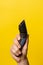 Close up on hand of unknown caucasian man holding electric beard trimmer cordless hair cutter in front of modern yellow background