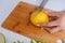 Close-up of hand unrecognizable woman cutting fresh lemon using kitchen knife on board.