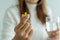 Close up of hand of woman holding a dietary supplement or medication or vitamin and a glass of water ready to take.