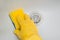 Close-up of a hand in a yellow rubber glove wipes a white sink with a sponge.