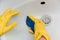 Close-up of a hand in a yellow rubber glove wipes a white sink with a sponge.