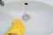 Close-up of a hand in a yellow rubber glove wipes a white sink with a sponge.