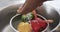 Close up of hands of african american woman rinsing vegetables in kitchen sink, in slow motion