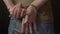 Close-up of hands behind the back handcuffed. Dark background.